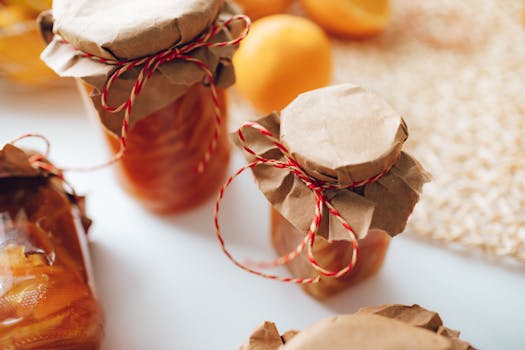 A close-up image of homemade preserves in jars wrapped with paper and string, indoors.